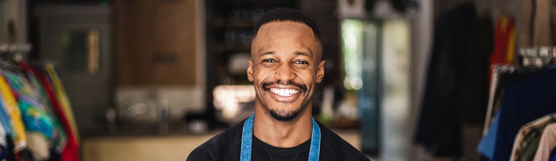 A man smiling in the center of a small clothing store.