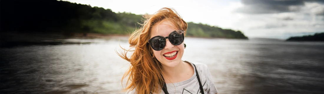 A woman smiling outside in front of a lake.